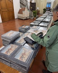 Eine lange Tischreihe mit Büchern bepackt, eine Frau von hinten, die in einem Buch blättert.