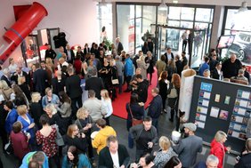 Blick von der Treppe des Kinos auf das Foyer, in dem viele Menschen stehen, sich unterhalten und Sekt trinken.