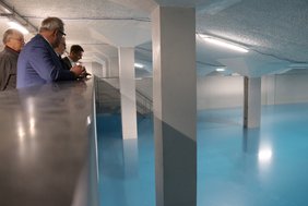 Das Bild zeigt ein sehr großes Wasserbecken. Der Oberbürgermeister und weitere Personen schauen über eine Brüstung auf das Wasser hinunter.