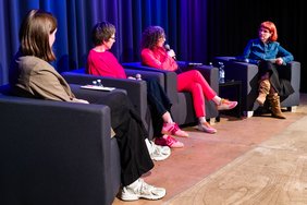 Das Podium in bequemen Lehnsesseln. Drei Teilnehmerinnen sind von hinten oder seitlich zu sehen. Die Moderatorin ist direkt gegenüber des Fotografen von vorne zu sehen