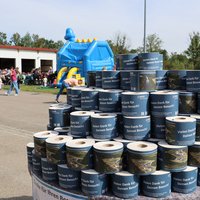 Im Vordergrund: auf einem Tisch sind hunderte Klopapierrollen gestapelt, versehen mit einer Banderole, die ein Luftbild des Gruppenklärwerks zeigt und die Aufschrift "Vielen Dank für Ihren Besuch". Im Hintergrund viele Besucher bei der Hüpfburg und der Gastronomie am Tag der offenen Tür. 