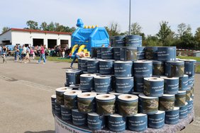 Im Vordergrund: auf einem Tisch sind hunderte Klopapierrollen gestapelt, versehen mit einer Banderole, die ein Luftbild des Gruppenklärwerks zeigt und die Aufschrift "Vielen Dank für Ihren Besuch". Im Hintergrund viele Besucher bei der Hüpfburg und der Gastronomie am Tag der offenen Tür. 