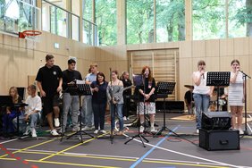 Schülerinnen und Schüler mit Mikros und Instrumenten in einer Ecke der Turnhalle.