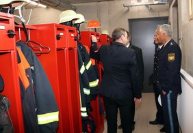 Einige Personen in einem Raum mit leuchtend roten Spinden, wo bereits Einsatzkleidung hängt.