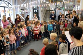 Im großen Kreis stehen Kinder und Erwachsene in der Stadtbibliothek. Darüber sind die Wimpelketten aufgehängt