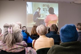 Viele Leute (es waren wohl 50 da, zu sehen ist nur ein Teil) von hinten zu sehen, vorne läuft auf einer Leinwand der Film.