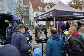 Viele Leute, darunter auch Kinder, stehen vor einem Monitor, auf dem das Bild, das die Drohne über dem Platz aufnimmt, direkt zu sehen ist